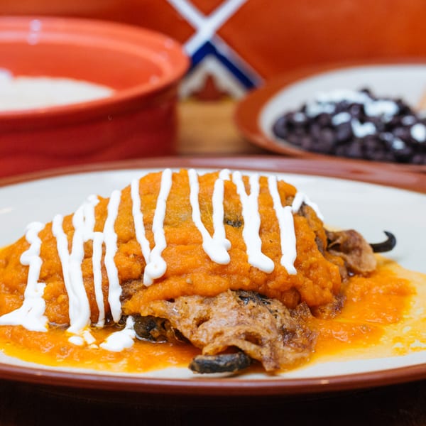 Frida Cantina's chile relleno, topped with orange sauce and white crema, with rice and beans in the background.